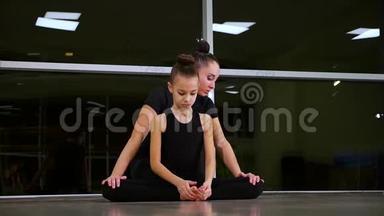 两个身材苗条、可爱的女孩姐妹，穿着黑色运动服的<strong>艺术体操</strong>运动员，在健身房做热身运动，做肌肉伸展运动